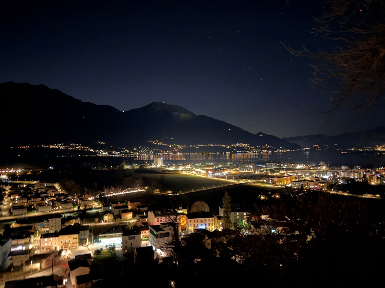 Panorama notturno con lago, montagne e luci del territorio